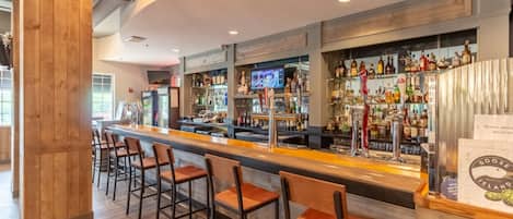 Zona de bar con una barra larga, varios taburetes y una amplia selección de botellas y vasos.