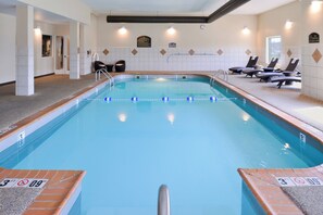 An indoor swimming pool with clear water, marked depth lines, and lounge chairs along the side.
