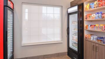 A room with a refrigerator, a window, and shelves stocked with snacks.