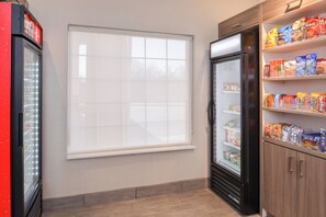 A room with a refrigerator, a window, and shelves stocked with snacks.
