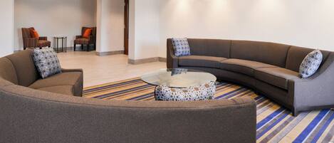 Un vestíbulo moderno con un sofá modular curvo, una mesa de centro de vidrio y dos sillones.