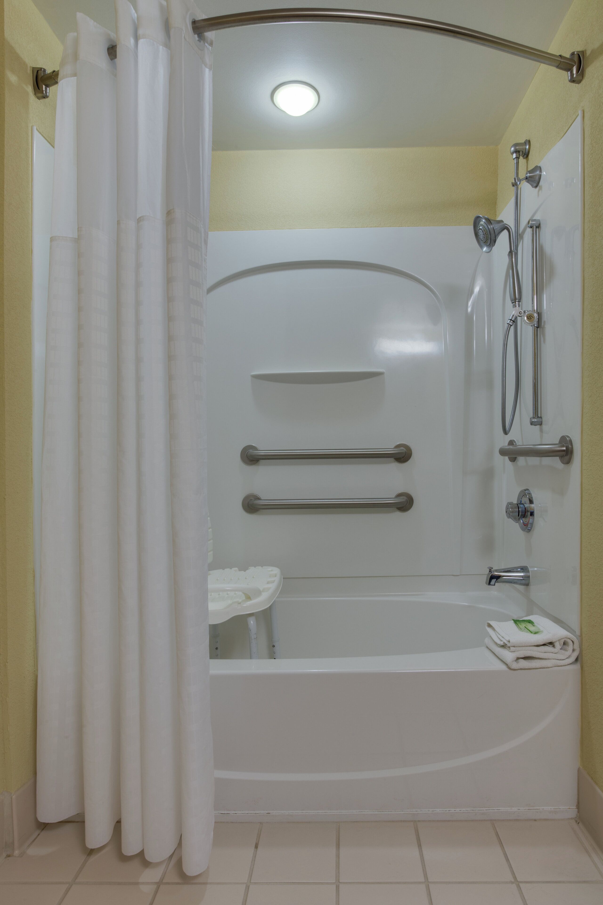 A bathroom with a bathtub, shower, and handrails.