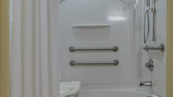 A bathroom with a bathtub, shower, and handrails.