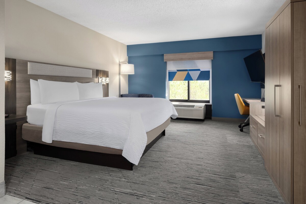 Een hotelkamer met een groot bed, een bureau, een stoel, een televisie en een raam met uitzicht.