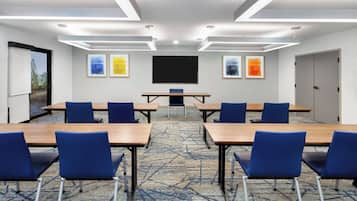 A conference room with a large table, blue chairs, a projector screen, and framed artwork on the walls.