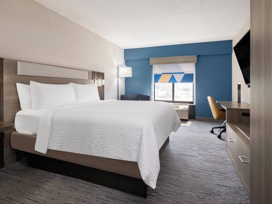 A hotel room with a large bed, a desk, a chair, a TV, and a window with blinds.