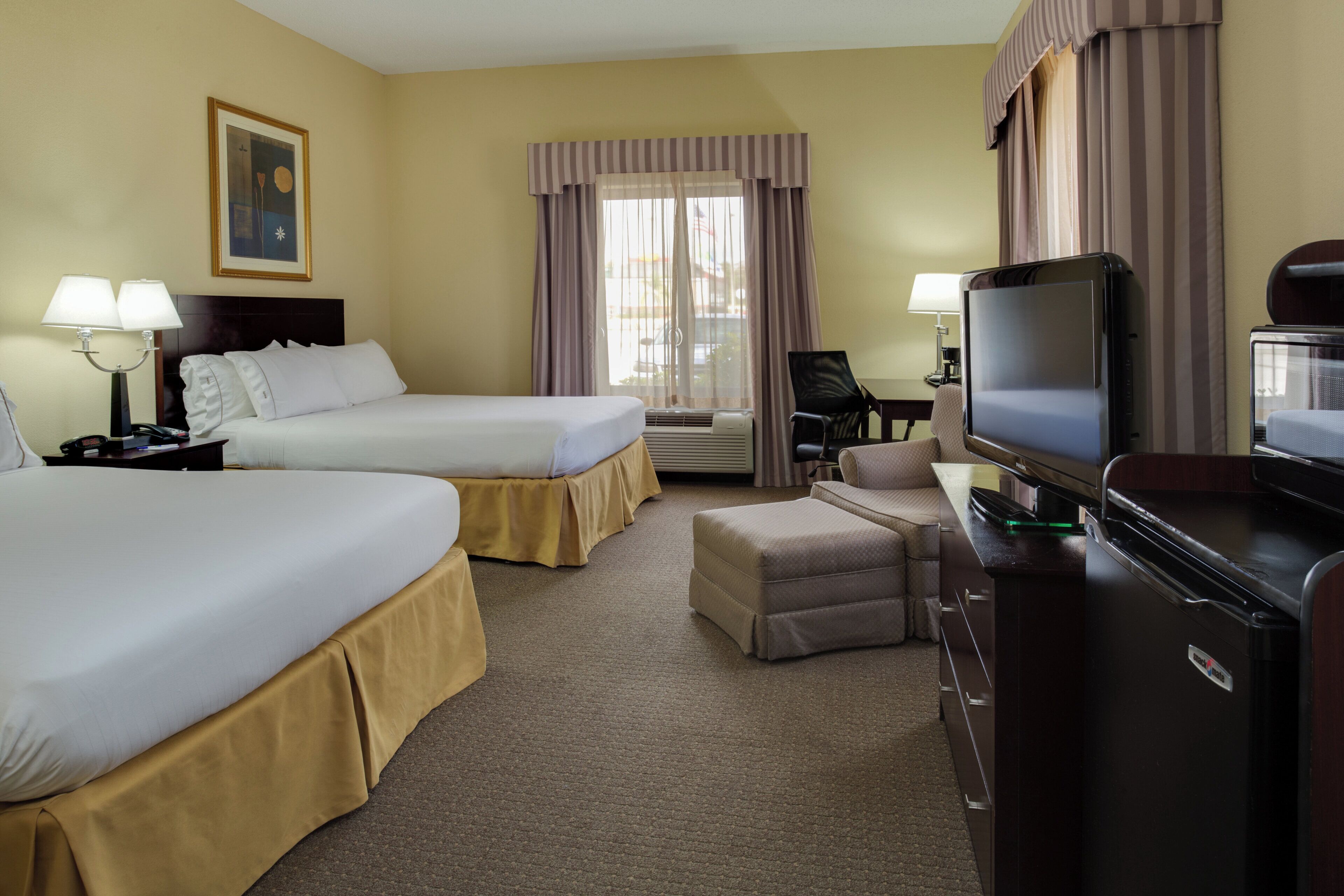 A hotel room with two beds, a desk with a television, and a chair.