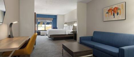 Un cuarto de hotel con una cama, un sofá azul, un escritorio de madera con una silla, una mesa de centro y un cuadro en la pared.