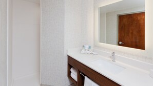 Un baño moderno con lavamanos blanco, tocador de madera y un espejo grande.