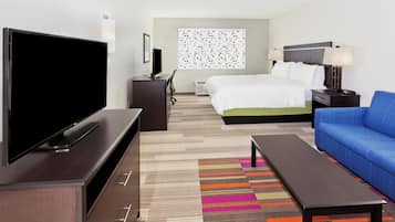 A hotel room with a television, a bed, a desk, a chair, a sofa, and a colorful rug.