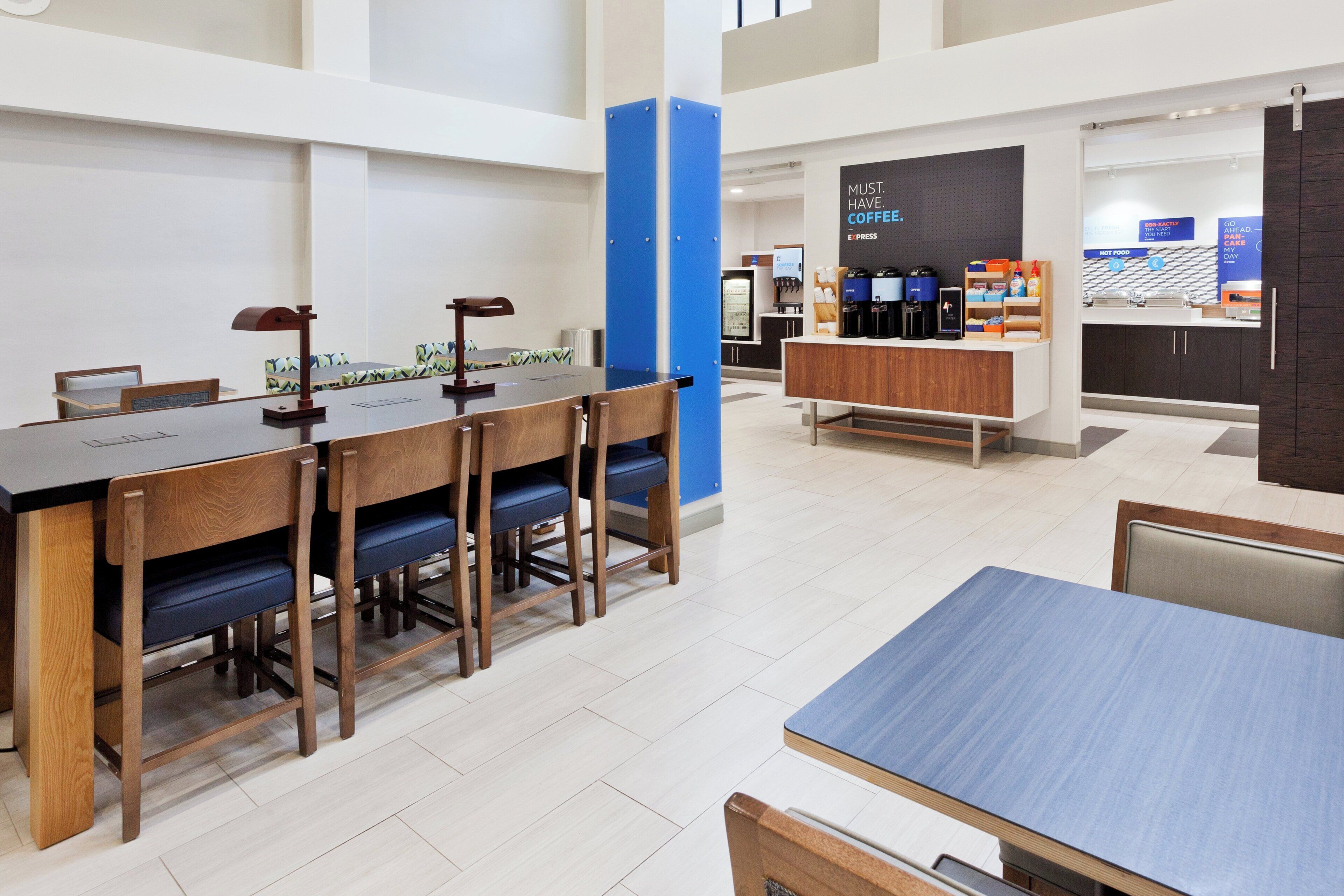 A modern dining area with a long wooden table and chairs, a coffee station, and a counter with various food items.