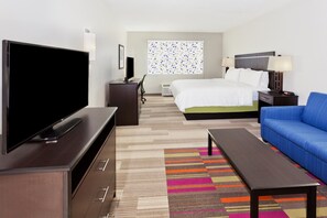 Une chambre d’hôtel avec un lit, une télévision, un bureau, une chaise, un canapé et un tapis coloré.