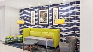 Een moderne zithoek met een bank, fauteuils, een ronde tafel en een behang met een patroon.