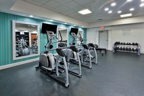Un gimnasio con cintas de correr, un espejo grande y un estante con mancuernas.