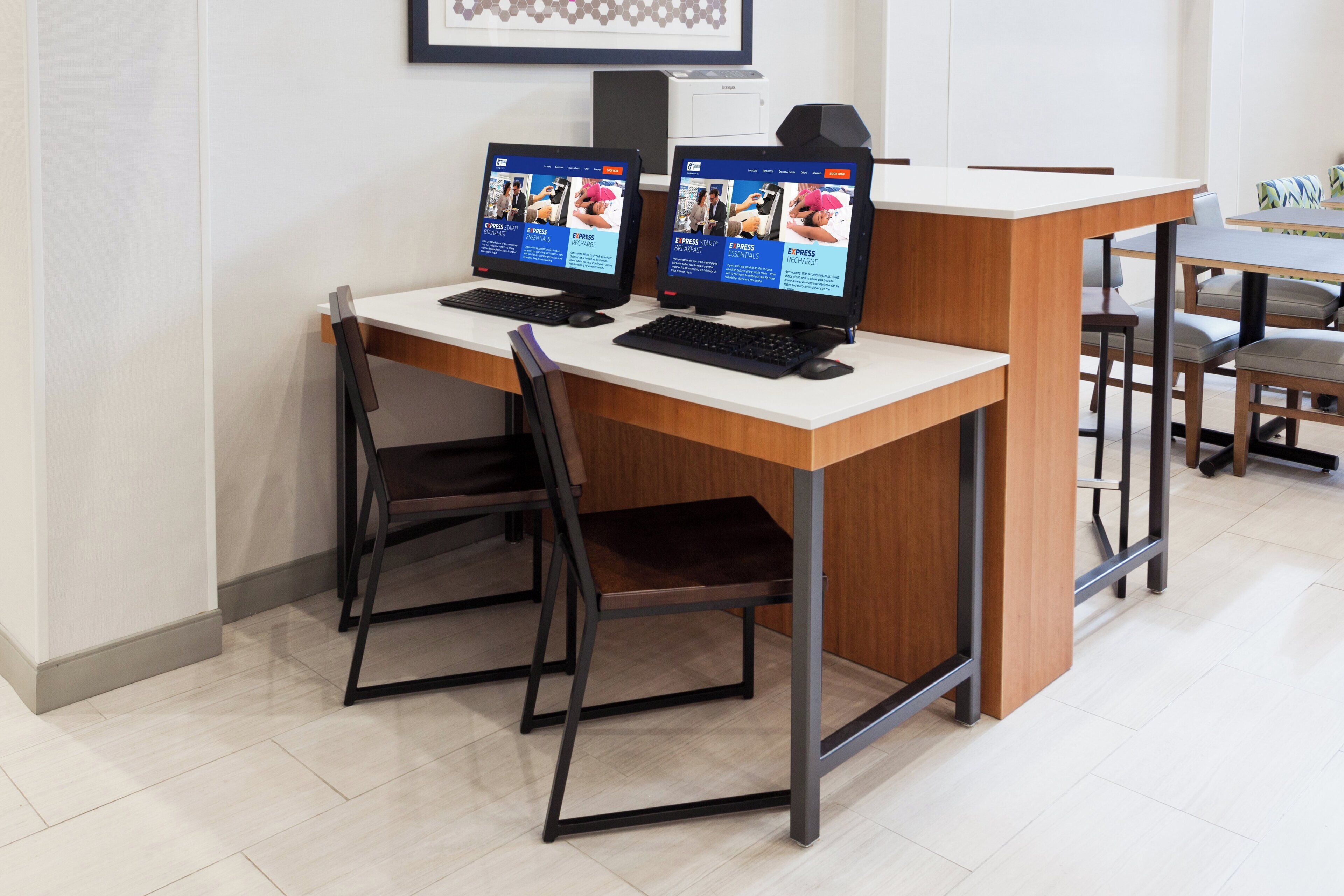 Un espace d’accueil comprenant deux postes de travail informatiques, un comptoir de réception blanc et un coin salon avec des chaises.