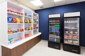 A snack and beverage vending area with shelves stocked with various snacks and a freezer with bottled drinks. - Holiday Inn Express Hotel & Suites Montgomery E - Eastchase by IHG (Montgomery)