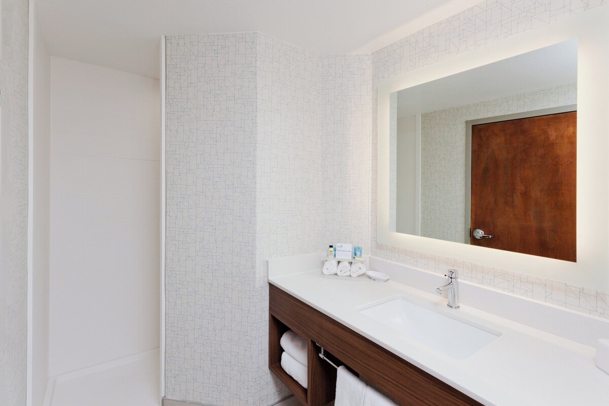 Une salle de bain avec un lavabo blanc, un meuble-lavabo en bois et un miroir dont le cadre est en bois.