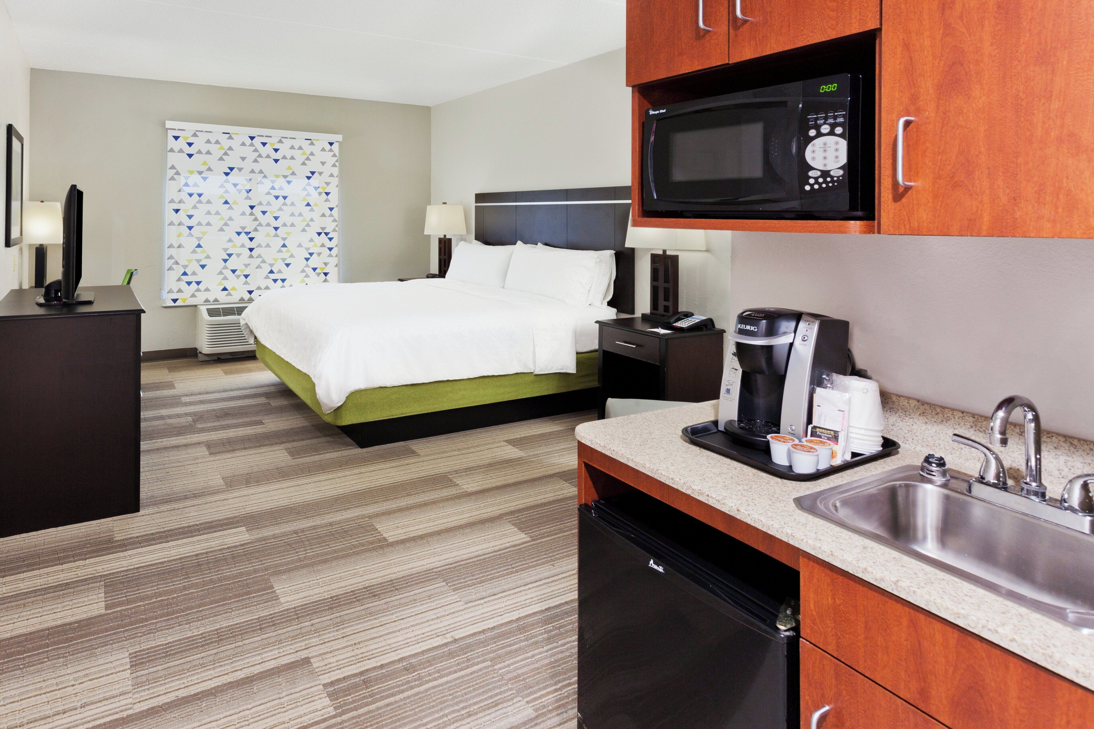 A hotel room with a bed, a desk, a microwave, a coffee maker, and a sink.