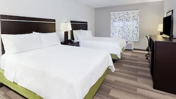 Habitación de hotel con dos camas, un escritorio, un televisor y una ventana con un diseño geométrico.