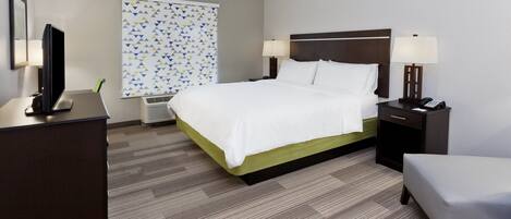 Habitación de hotel con cama, mesitas de noche, escritorio, silla y ventana con cortinas estampadas.