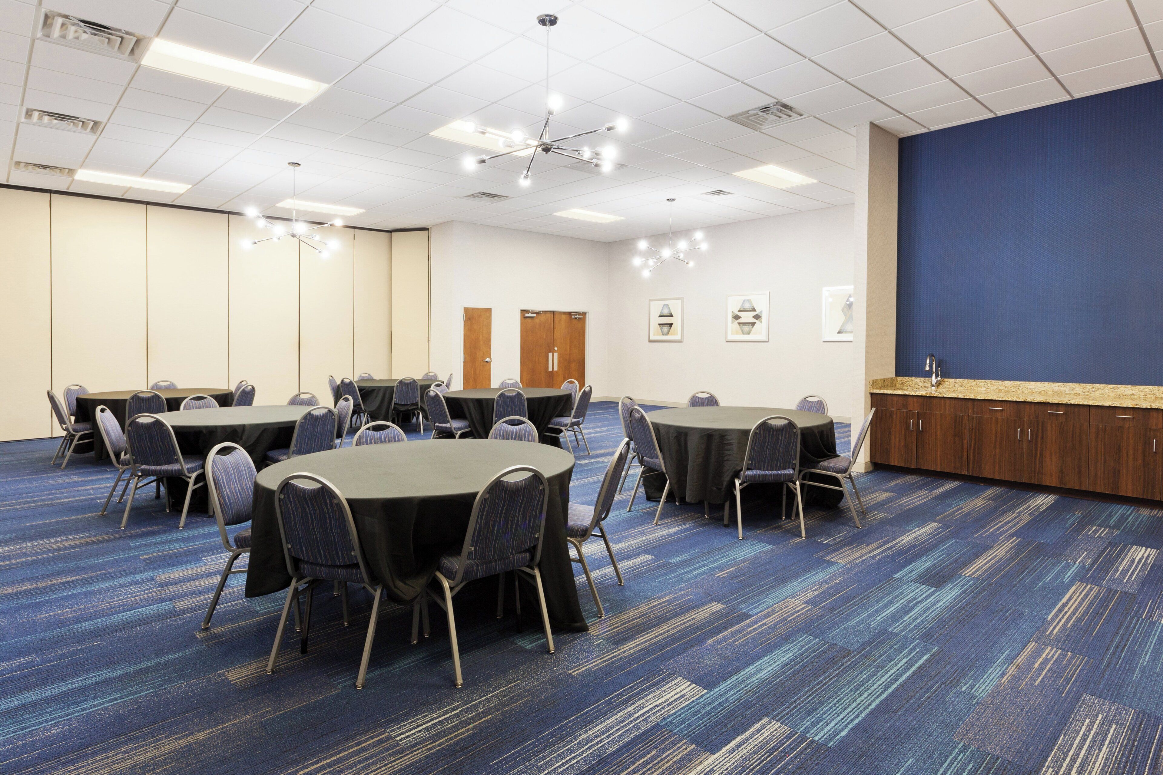 Une salle de conférence équipée de plusieurs tables et chaises, d’un coin cuisine et d’un grand mur bleu.