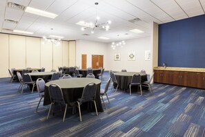 A conference room with multiple tables and chairs, a kitchenette area, and a large blue wall. - Holiday Inn Express Hotel & Suites Montgomery E - Eastchase by IHG (Montgomery)