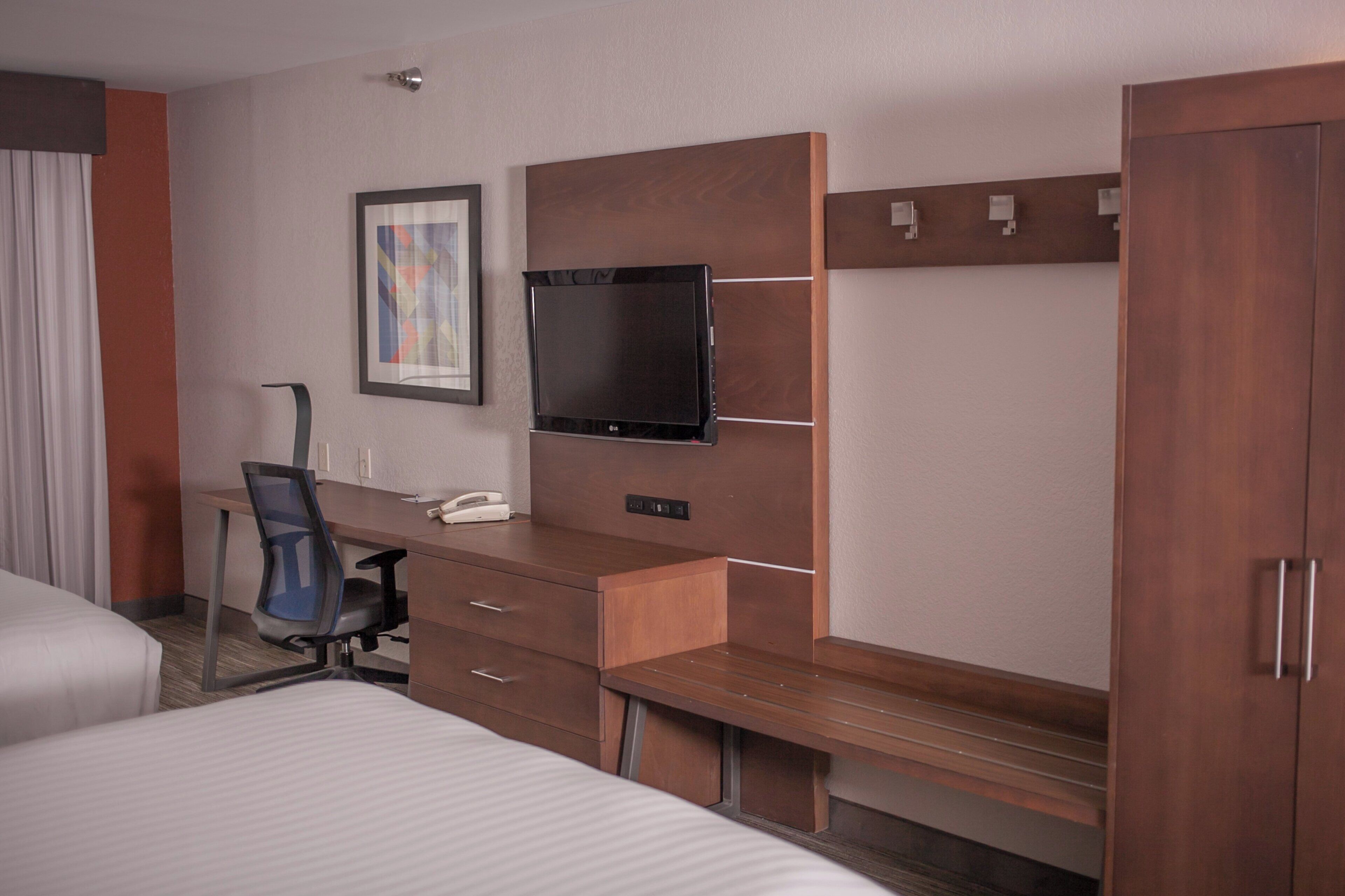 Una habitación de hotel con una cama, un escritorio con una silla, un televisor y un armario.