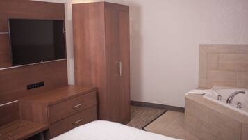 A hotel room with a bed, a wooden wardrobe, a TV mounted on the wall, and a bathroom with a bathtub and sink.