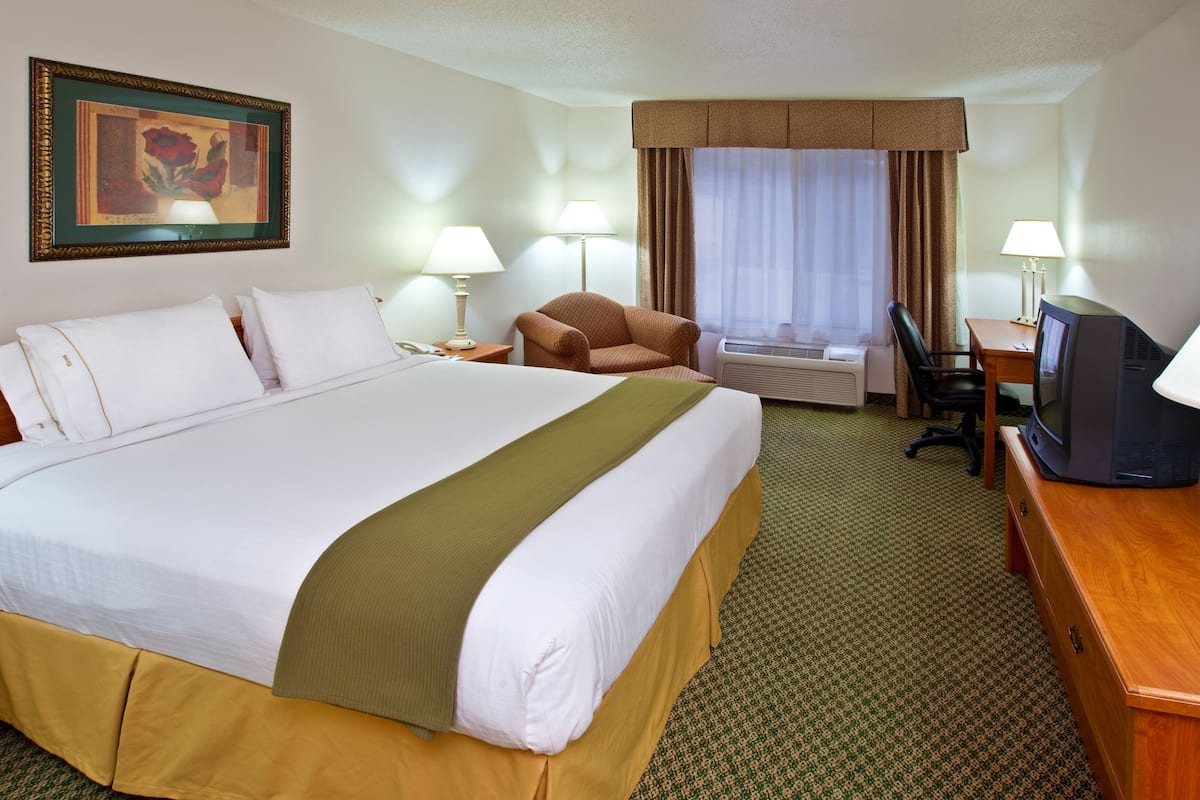 A hotel room with a large bed, a desk with a television, a chair, and two lamps.