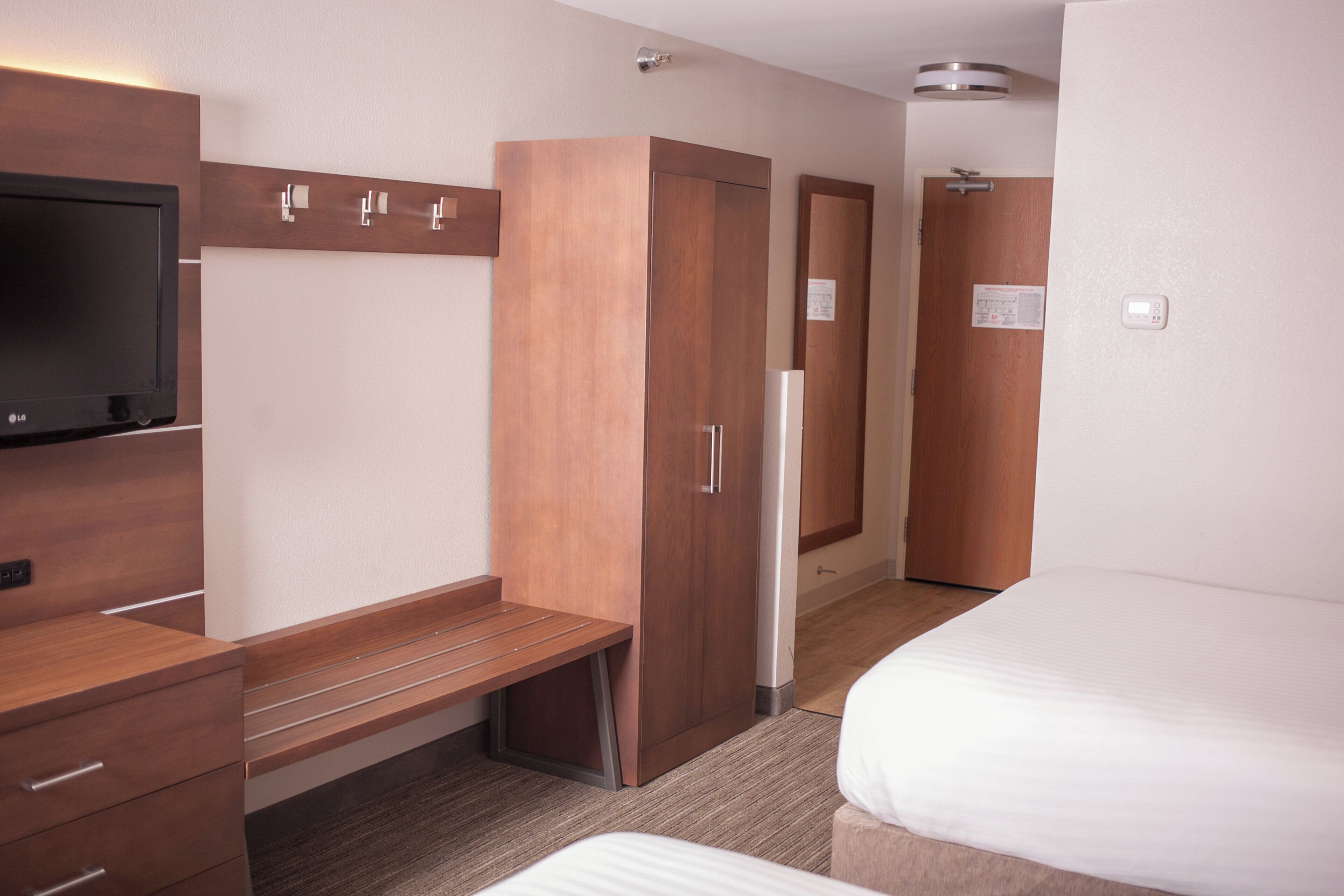 A hotel room with a bed, a desk with drawers, a TV, and a wardrobe.