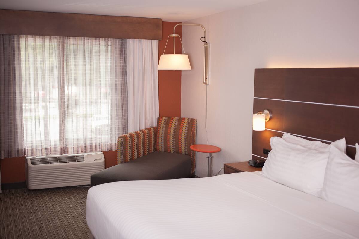 Ett hotellrum med en stor säng, en liten soffa, ett runt bord, en lampa och ett fönster med gardiner.