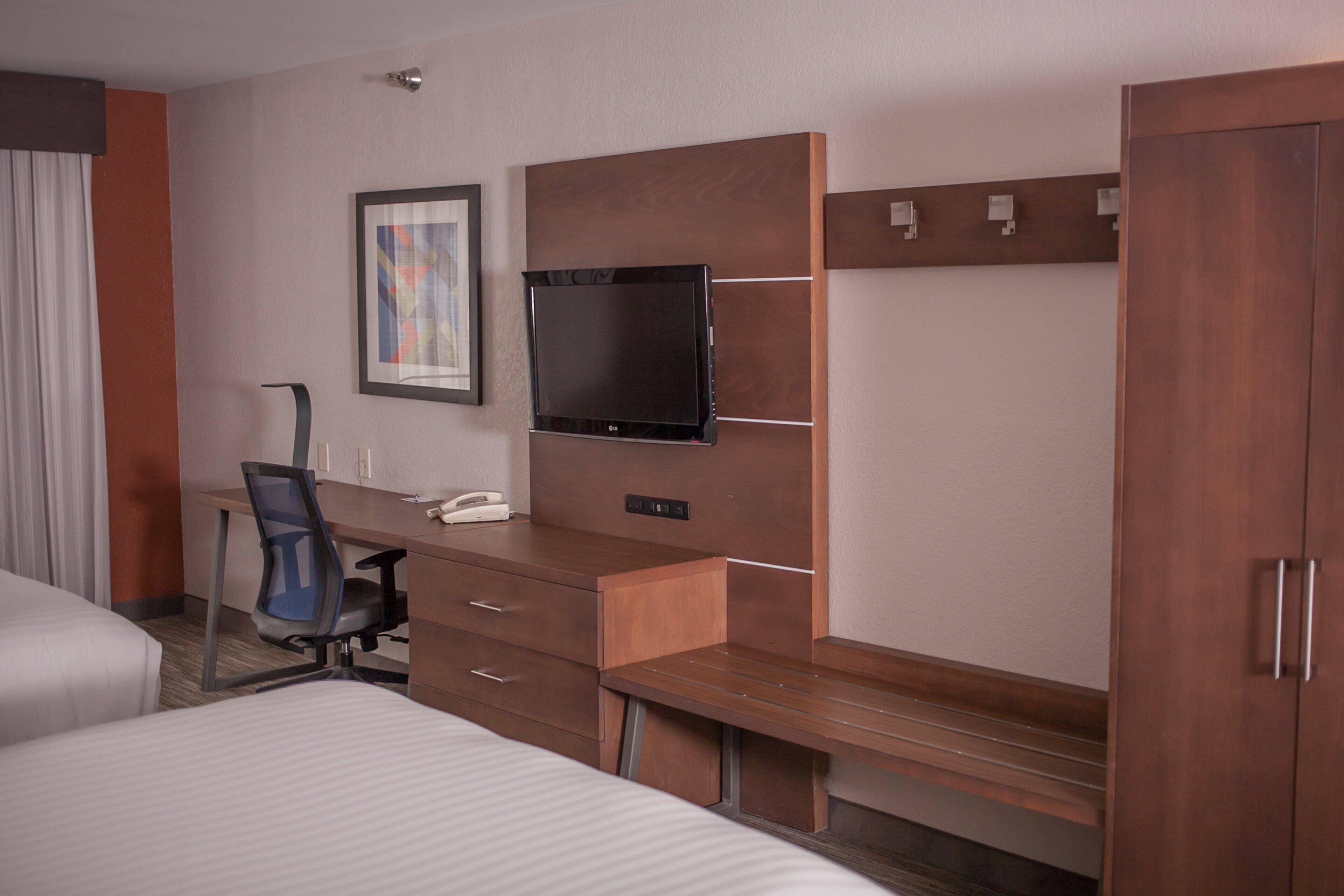 Una habitación de hotel con cama, escritorio con silla, televisor y armario.