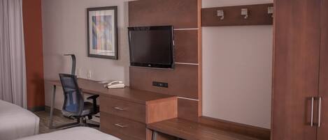 Una habitación de hotel con cama, escritorio con silla, televisor y armario.