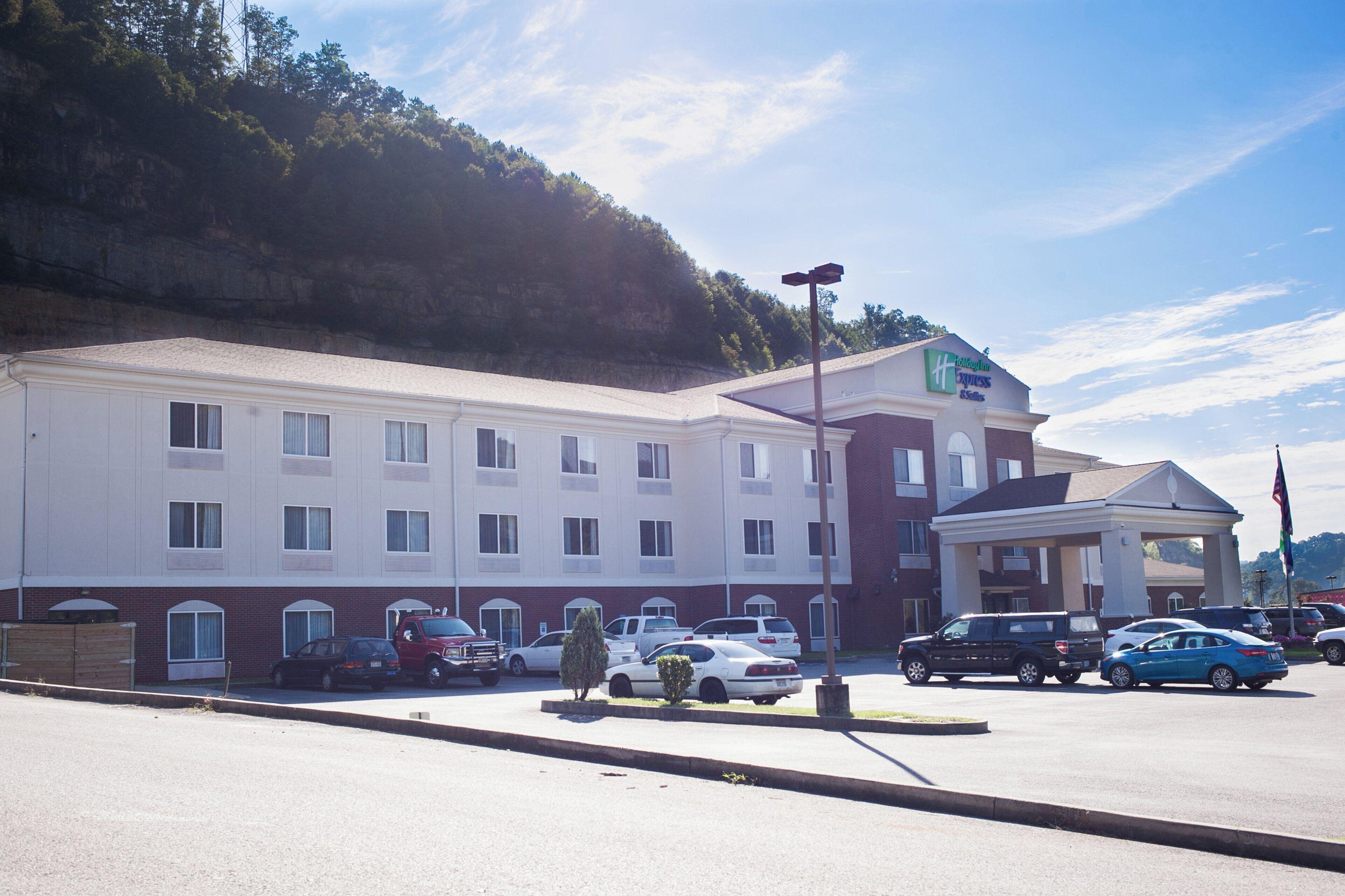 Il s’agit d’un hôtel à plusieurs étages, doté d’un toit plat et d’une enseigne indiquant qu’il s’agit d’un Holiday Inn Express & Suites. Plusieurs voitures sont garées devant, et on peut voir un mât sur lequel flotte un drapeau américain.