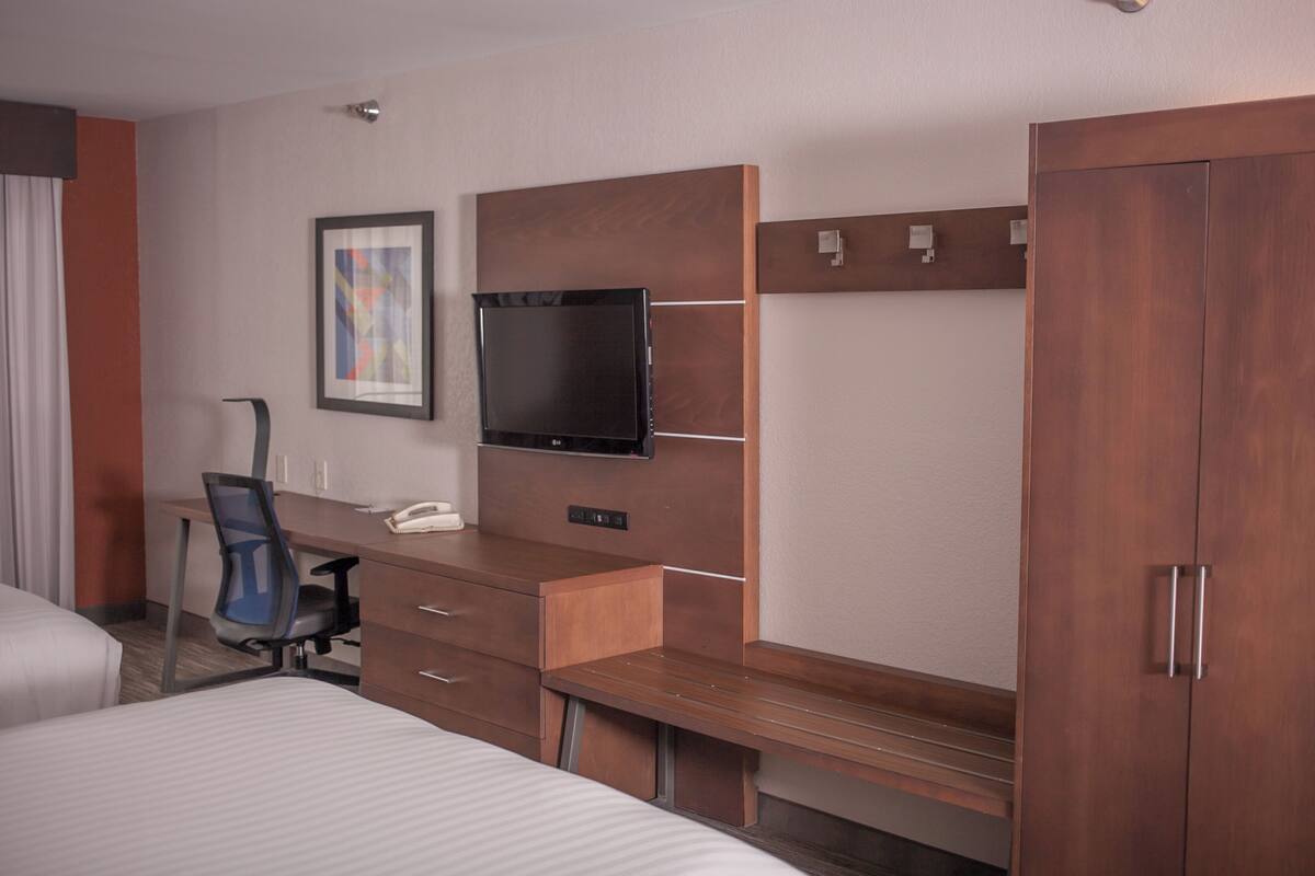 Ett hotellrum med en säng, ett skrivbord med en stol, en tv och en garderob.