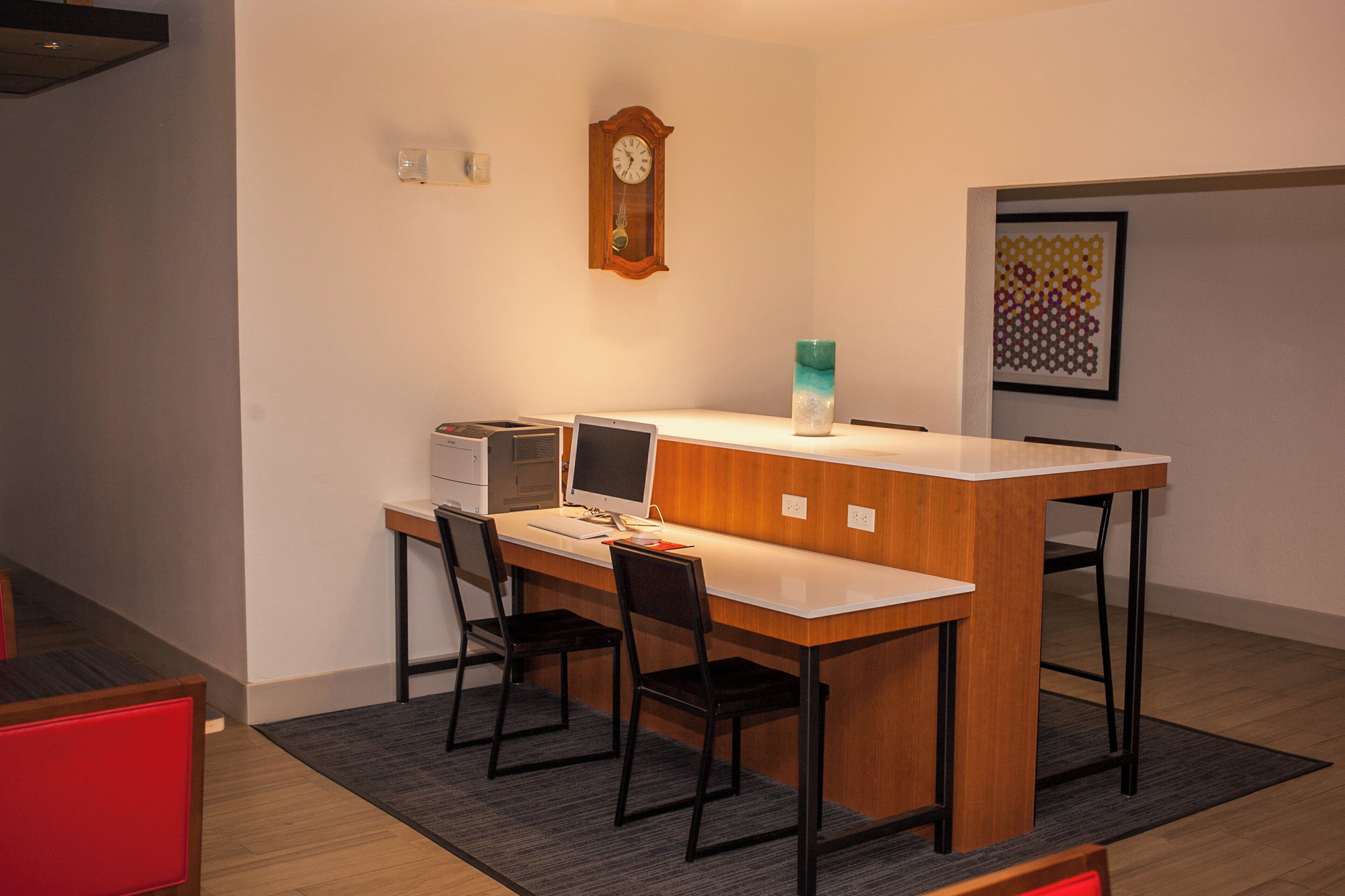 A small, modern kitchen with a wooden countertop, two chairs, a computer, and a clock on the wall.