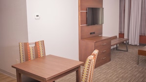 A hotel room with a wooden dining table, two chairs, a TV mounted on a wooden cabinet, and a small desk with drawers. - Holiday Inn Express Hotel & Suites by IHG (Logan)