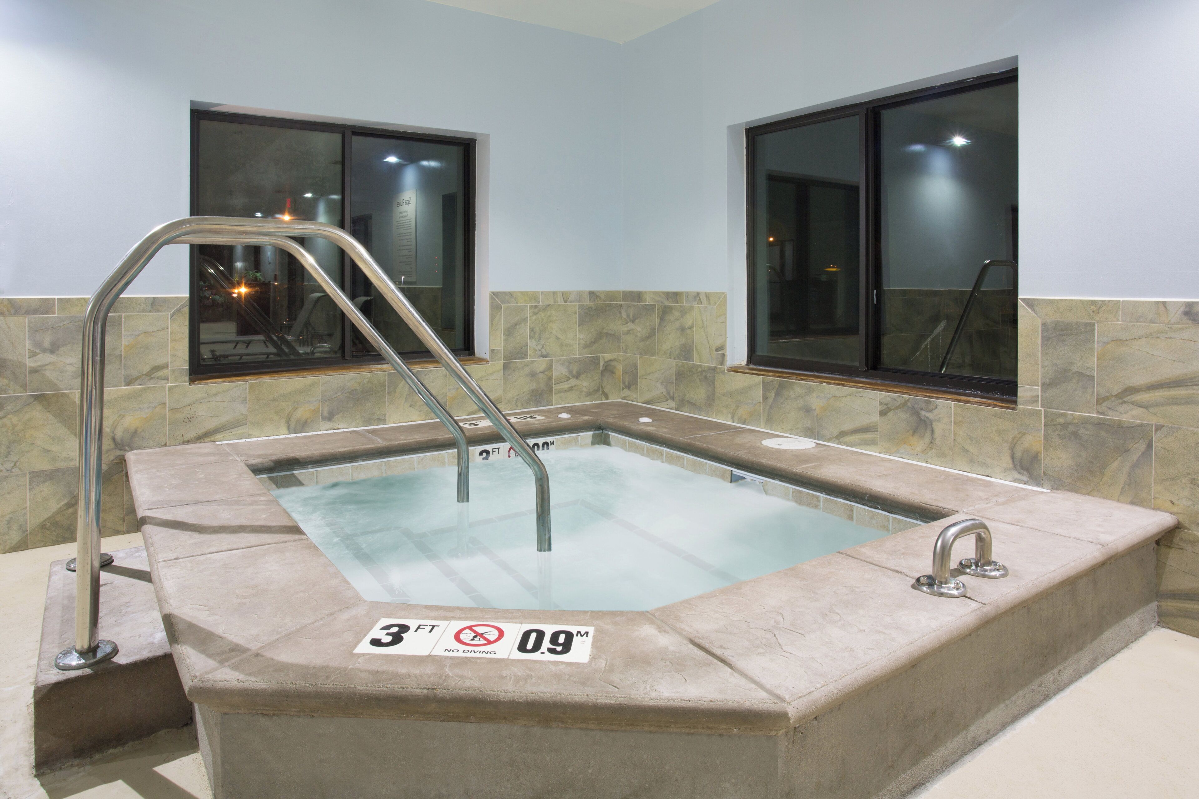 A rectangular hot tub with a metal ladder, a depth marker of 3 feet, and a no diving sign.