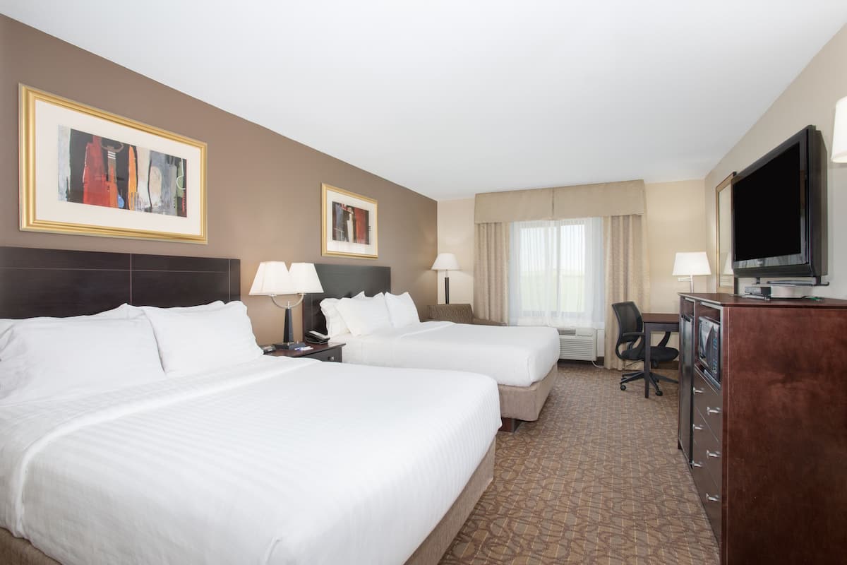 A hotel room with two beds, a desk, a television, and two framed pictures on the wall.