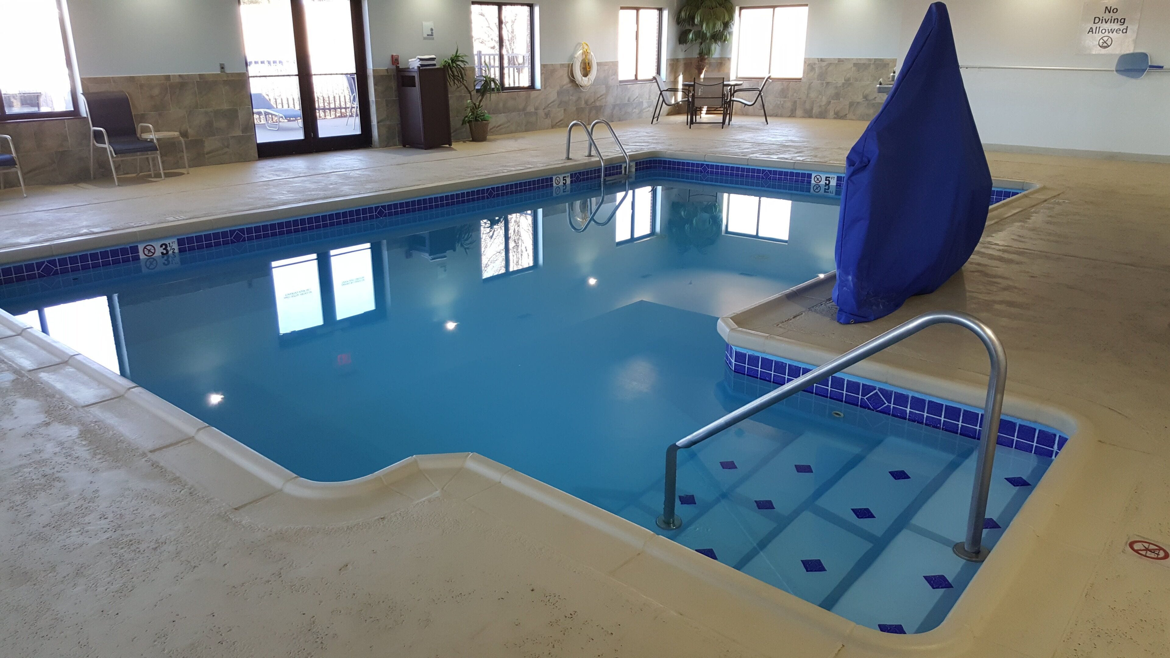 Una piscina interior con borde de azulejos, una silla de socorrista y un letrero que indica que no se permite el clavado.