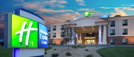Un hotel Holiday Inn Express & Suites con un cartel iluminado grande, césped bien cuidado y cielo despejado.