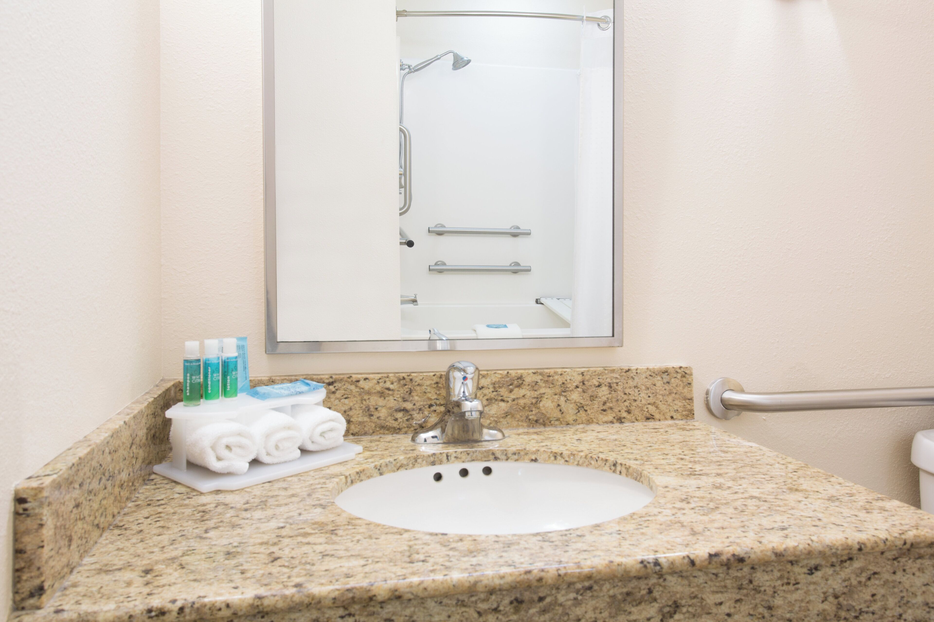 A bathroom with a granite countertop, a white sink, a mirror, and a shower enclosure.