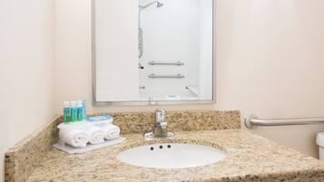 A bathroom with a granite countertop, a white sink, a mirror, and a shower enclosure.