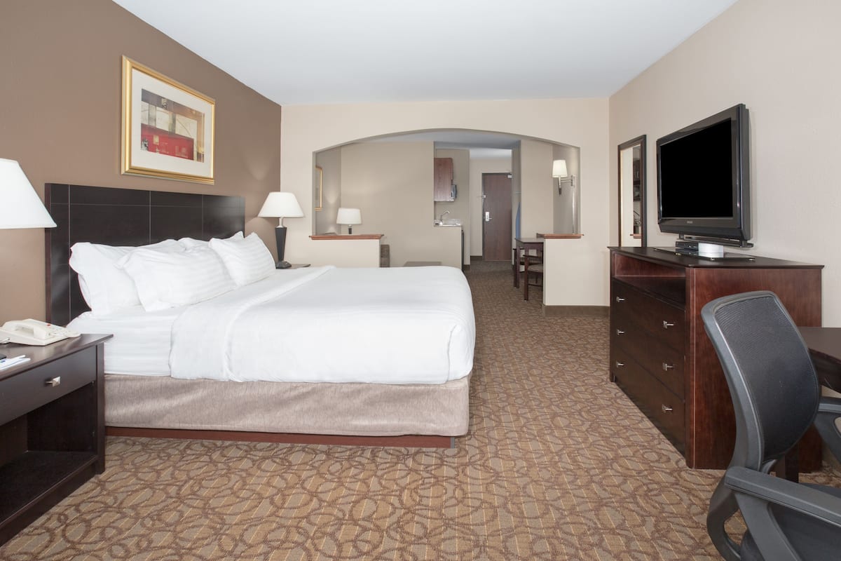 A hotel room with a large bed, a desk with a chair, a television, and a bathroom visible through an archway.