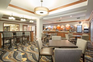 Un vestíbulo de hotel con una zona de bar, disposición de asientos y una cocina al fondo.