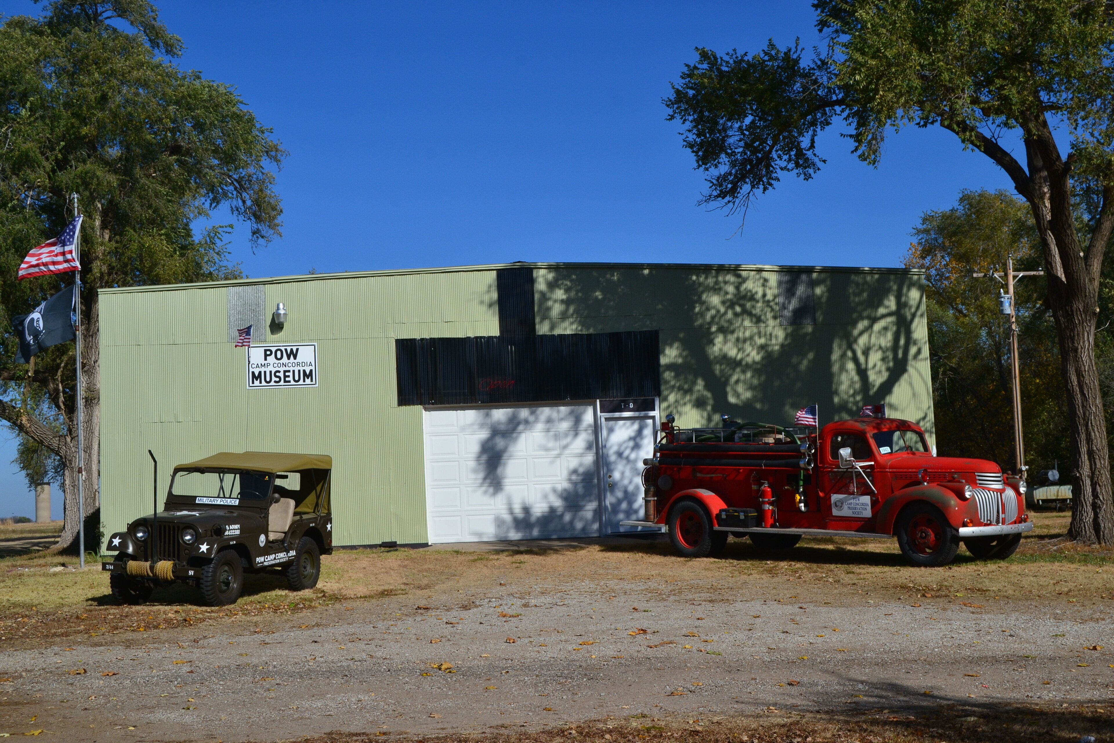 Un edificio con la scritta 'POW CAMP CONCORDIA MUSEUM', con un'antiqua autopompa rossa parcheggiata davanti.