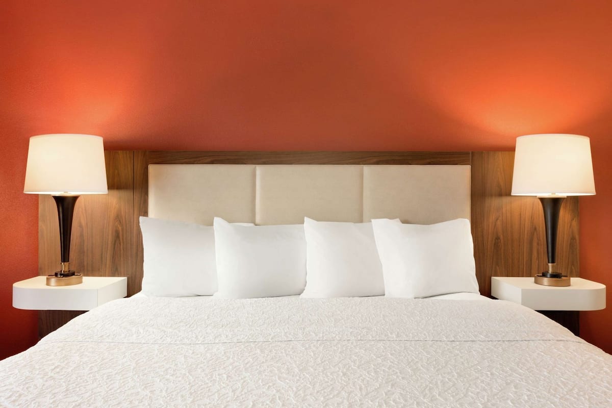 Una cama con colcha blanca texturizada, cabecera de madera y dos lámparas de noche.