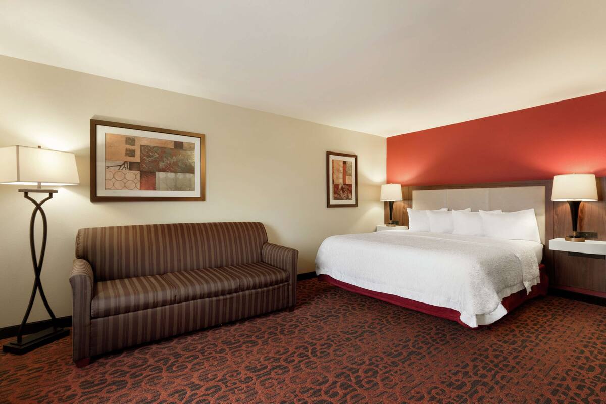 Una habitación de hotel con cama, sofá, dos lámparas fijadas a la pared y alfombra estampada.