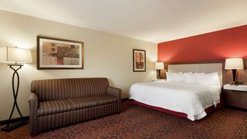 A hotel room with a bed, a sofa, two wall-mounted lamps, and a patterned carpet.