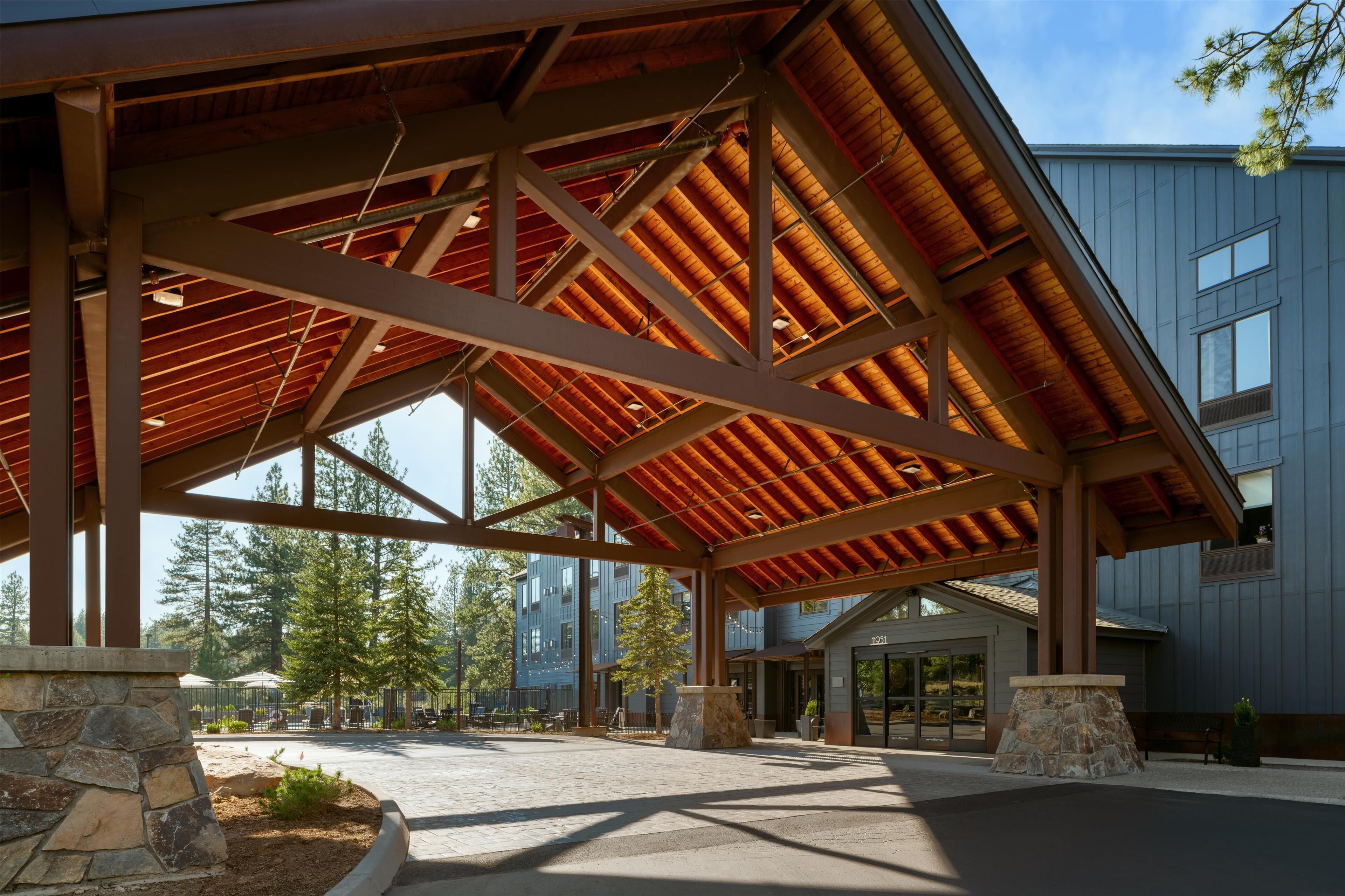 A covered outdoor area with a stone structure, a building with large windows, and a clear sky.